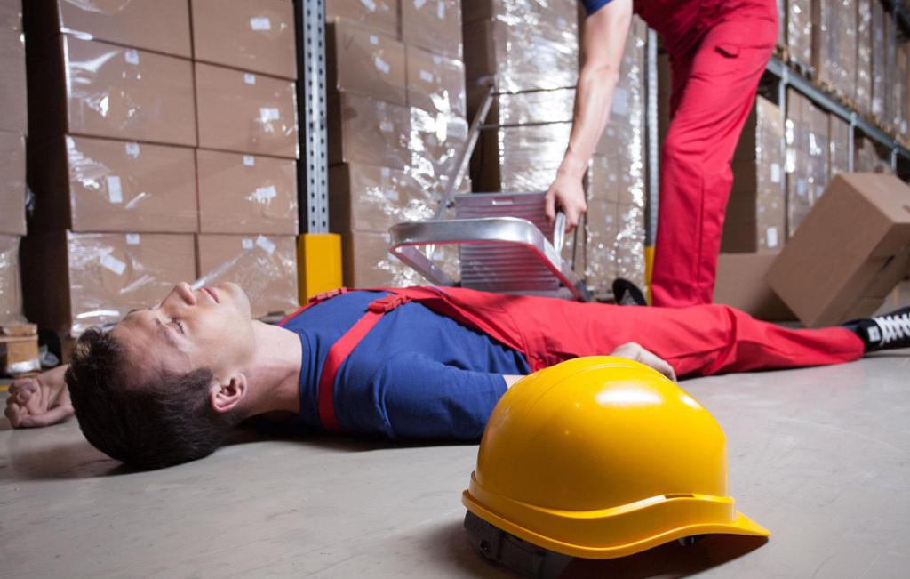 Person som har skadd seg på jobb og ligg på golvet med vernehjelm ved sida av. Foto