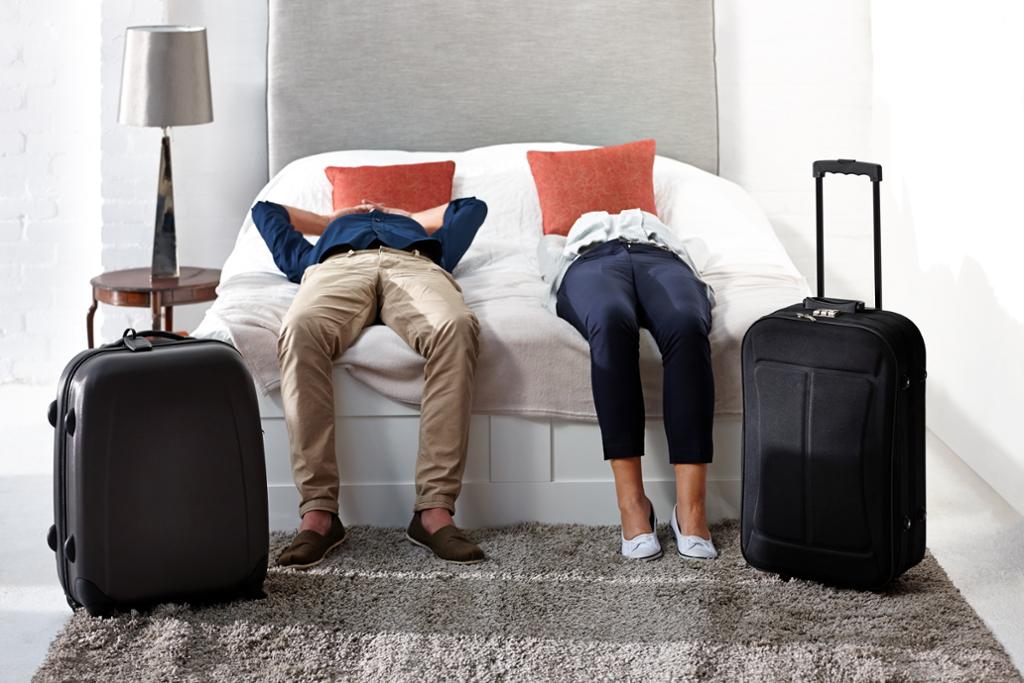 Par ligger utslitt på hotellseng. Foto.