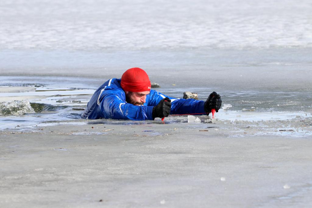 En mann  drar seg opp av ei råk i isen ved hjelp av ispigger. Foto.