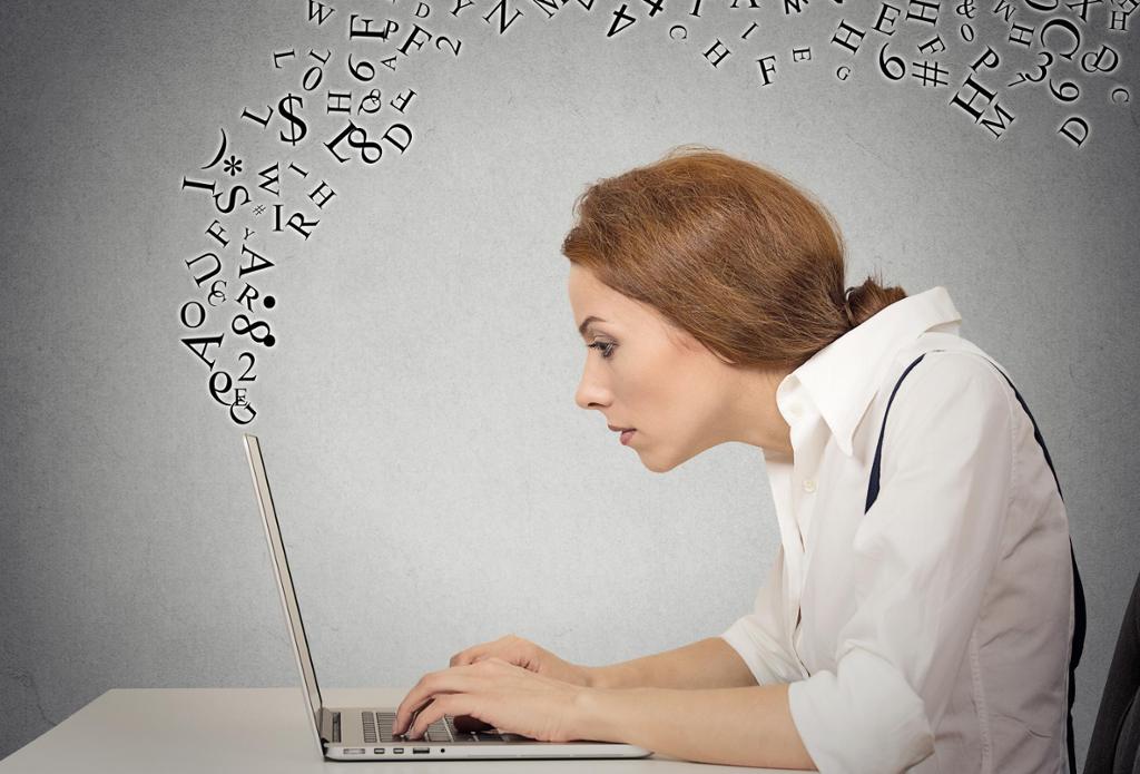 Kvinne skriver på sin bærbare datamaskin mens bokstaver flyr rundt. Foto.