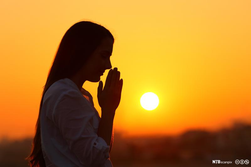 Kvinne ber i solnedgang. Foto.