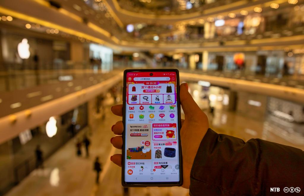 Ei hånd holder en mobil med mange fargerike apper. Skriftspråket er kinesisk. Foto. 