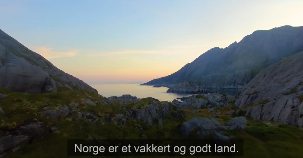 Landskap i kveldslys med fjord og fjell og underteksten: "Norge er et vakkert og godt land." Skjermbilde.