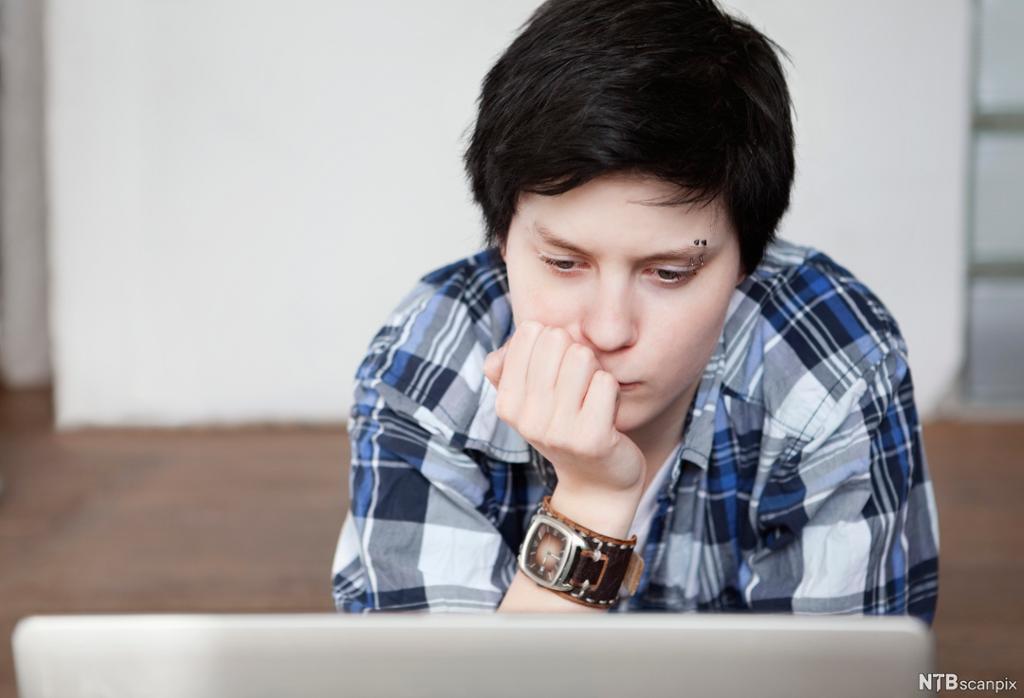 En ung person ser tankefullt på en dataskjerm. Foto.