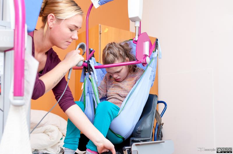 Barn med nedsatt funksjonsevne løftes i rullestol ved hjelp av spesialutstyr. Foto.