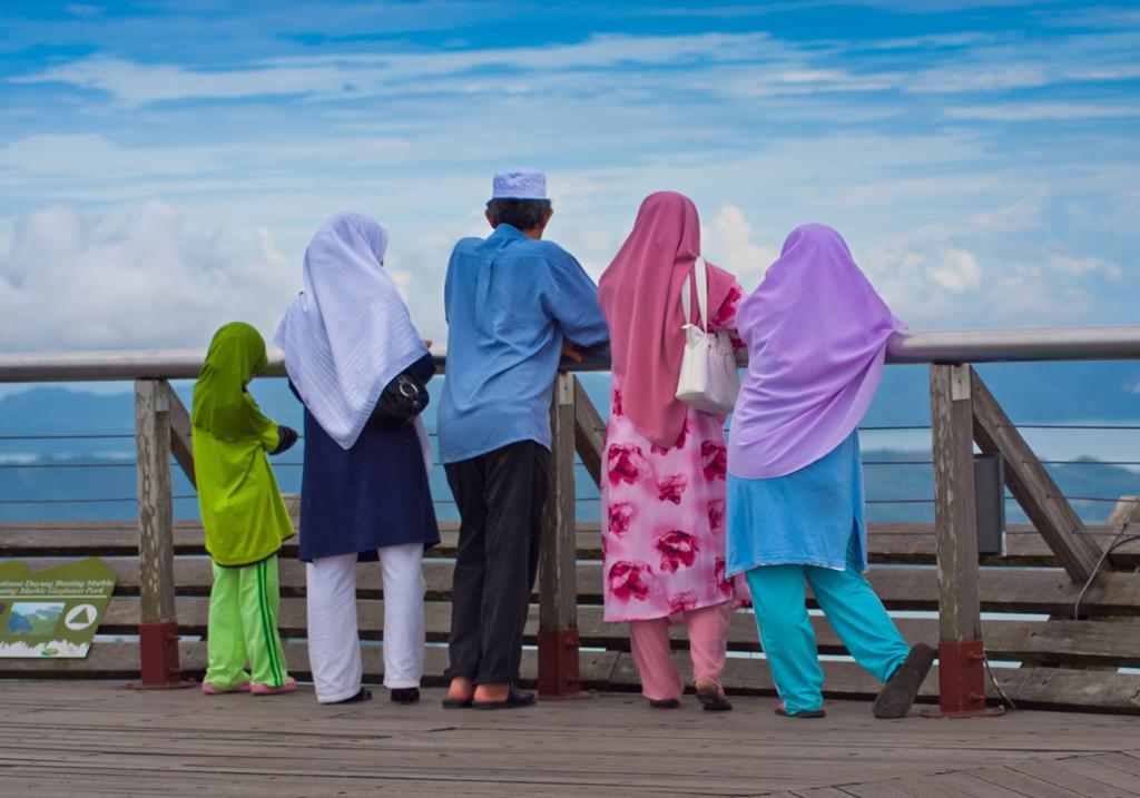 Muslim family in colorful clothes looking at the sea. Photo.