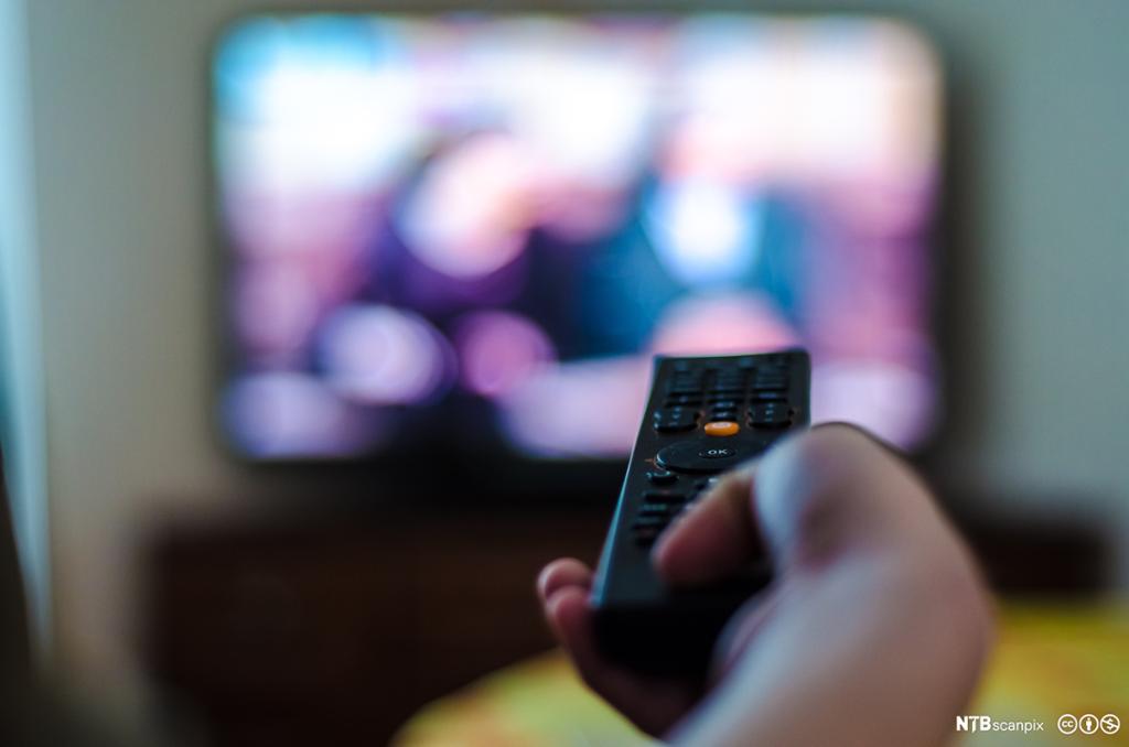 En hånd trykker på en kontroll for å velge TV-kanal. Bilde.
