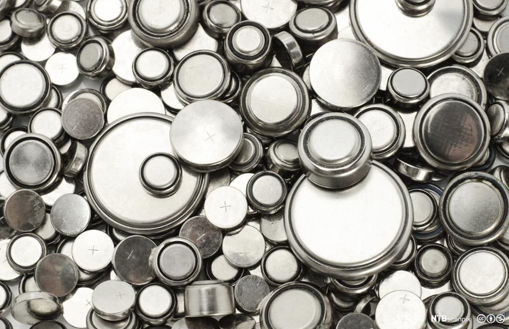 Store og små knappecellebatterier ligger spredt utover og fyller hele bildet. Foto.