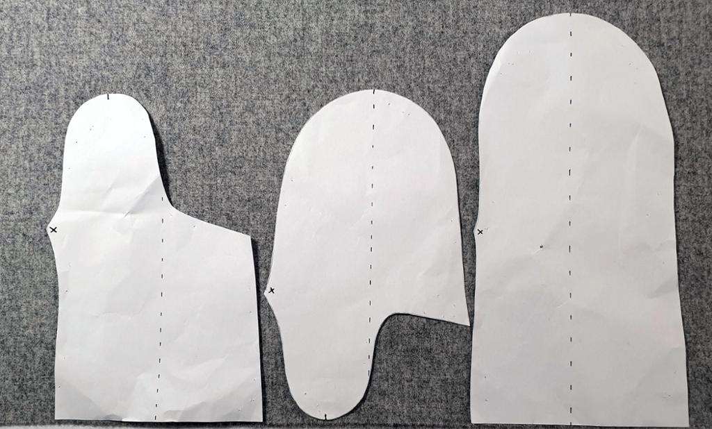 Fotografi av tre mønsterdeler i papir som ligger på et grått stoff. 