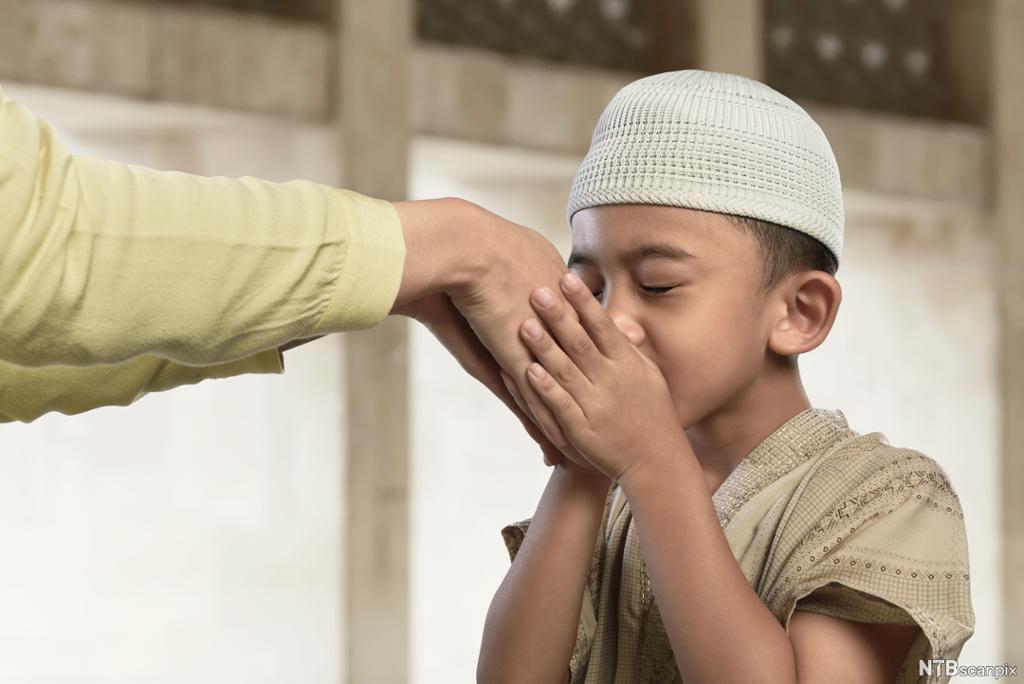 Asiatisk muslimsk gutt kysser en eldre manns hånd. Foto.