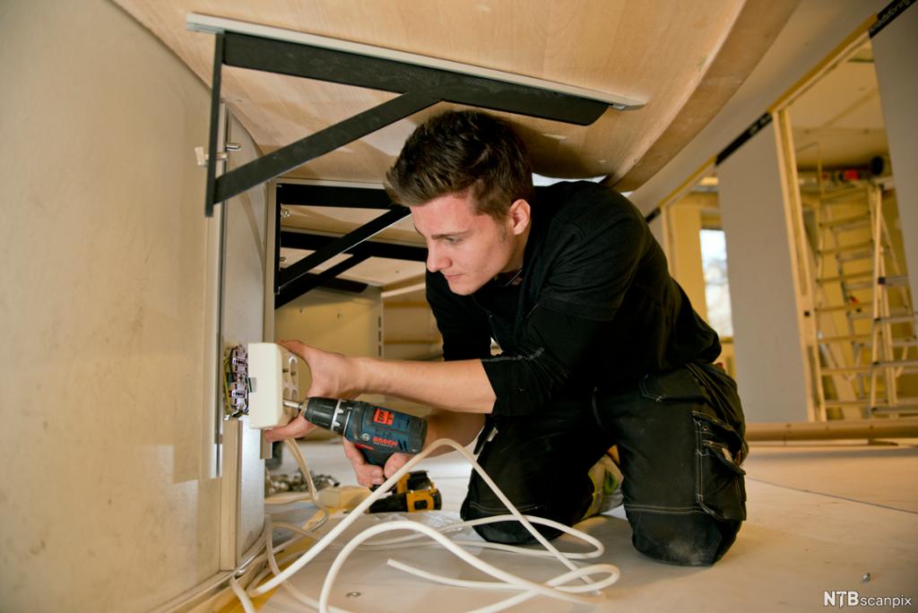Elektriker utfører åpen installasjon i kontorbygg. Foto.