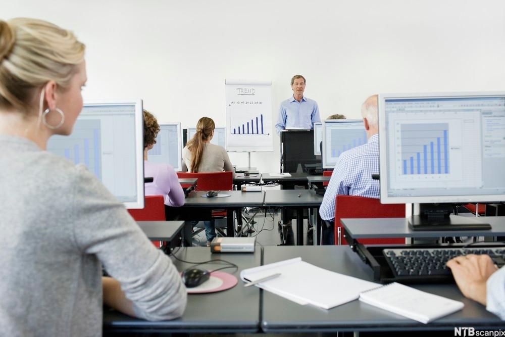 Kursdeltagere som sitter foran datamaskiner og får opplæring i et klasserom. Foto.