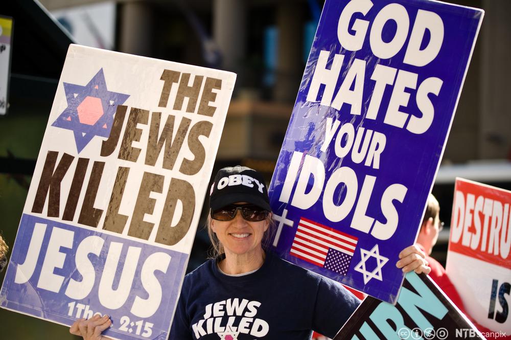 Kvinne som holder opp to plakater med jødefiendtlig innhold. Foto.