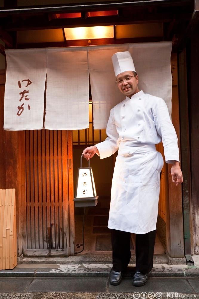Kokk foran inngang til japansk restaurant. Foto.