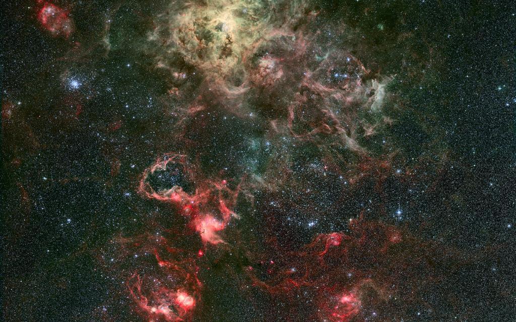 Stjernetåke framstilt i ein eksplosjon av raudfargar, gult og grønt på svart bakgrunn. Foto. 