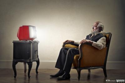 En gammel mann sitter i en stol og ser på er rødt plastikkfjernsyn. Foto.