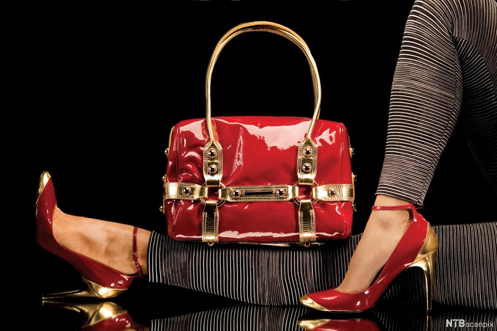 Ei skinnende, luksuriøs veske i rødt og gull og et par matchende sko. Foto. 