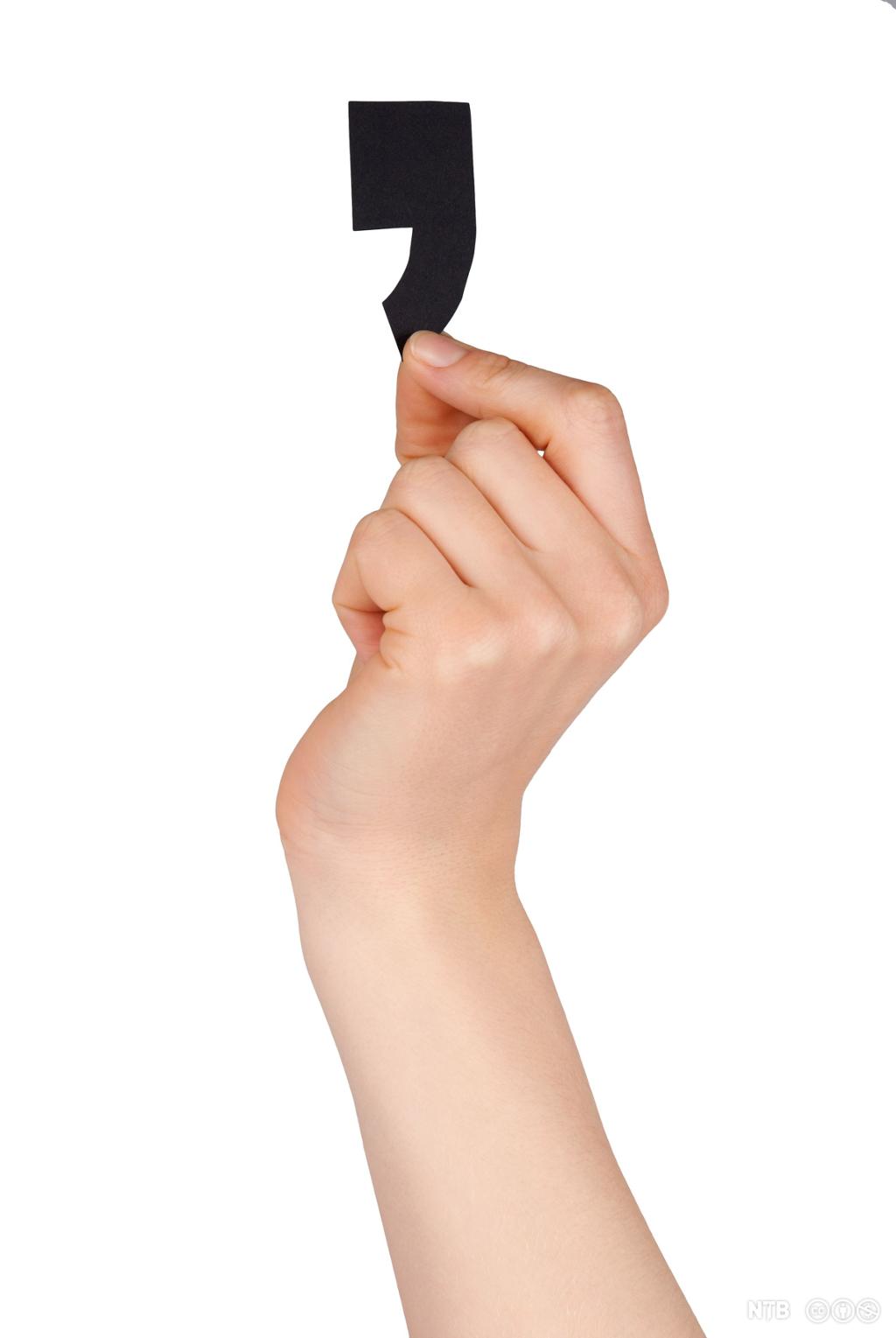 A hand holding up a black comma. Photo.