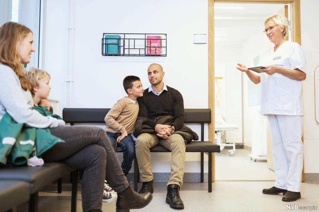 Ein sjukepleiar møter pasientar på venterommet på legekontoret. Foto.