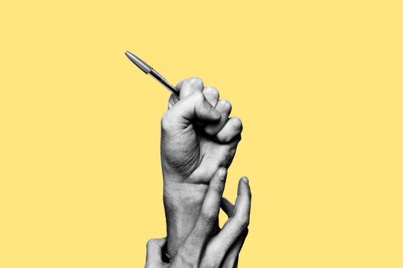 En hånd med penn blir dradd ned av en annen hånd. Gul bakgrunn. Foto.