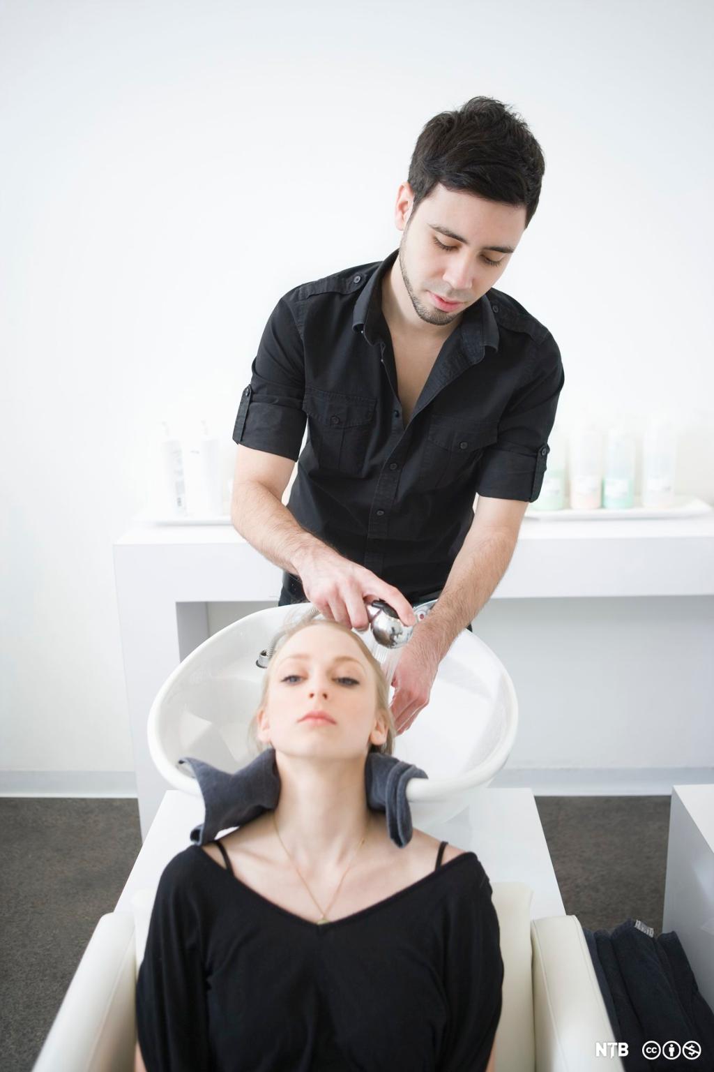 Mannleg frisør vaskar håret på ein kunde. Foto.