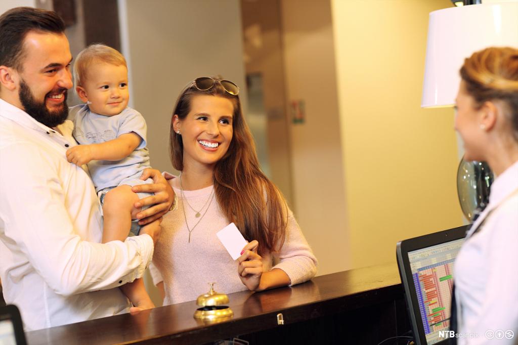 Et smilende par med en baby får nøkkelkort fra en hotellresepsjonist. Foto.