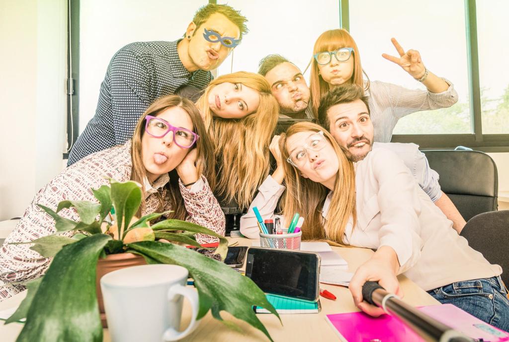 Sju personer på et kontor tar bilde med en selfiestang mens de gjør grimaser. Foto.