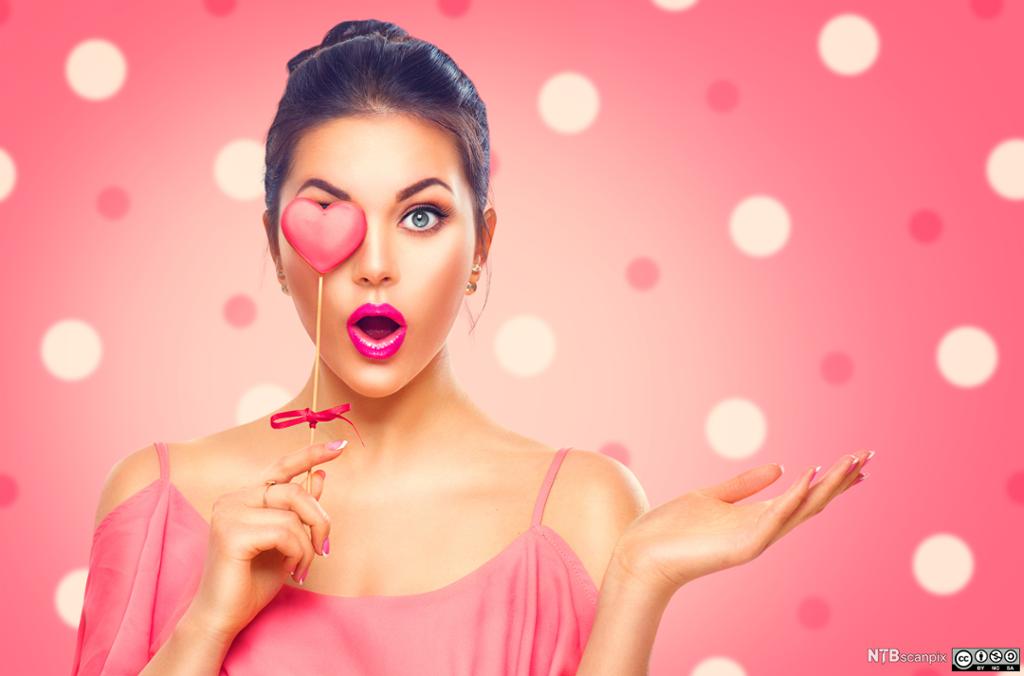 Woman in pink holding a heart-shaped lollypop. Photo. 