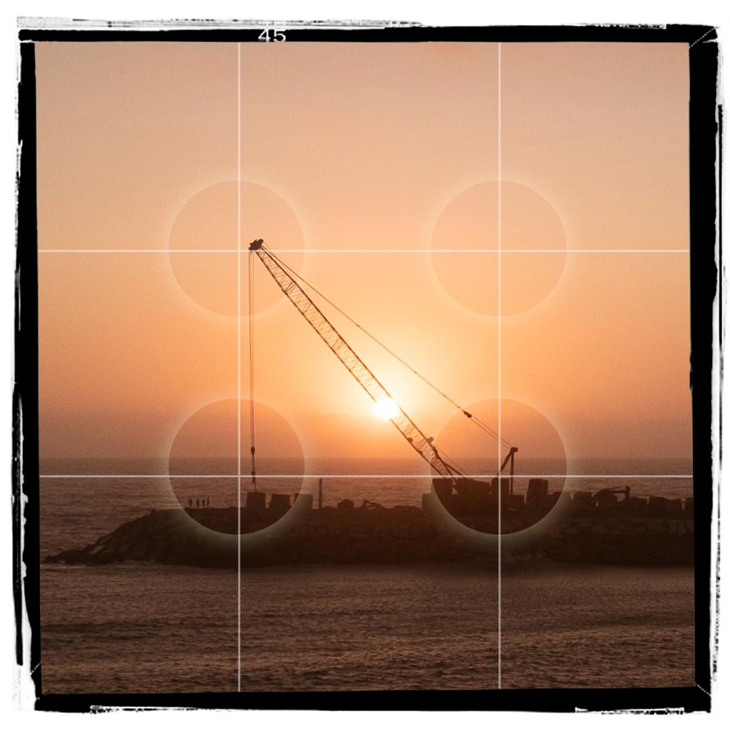 Bilde av heisekran i solnedgang, med rutenett som markerer tredelsregelen. Bildeflaten er delt i ni like store deler ved hjelp av to vertikale og to horisontale linjer, alle plassert i lik avstand fra hverandre. Foto.