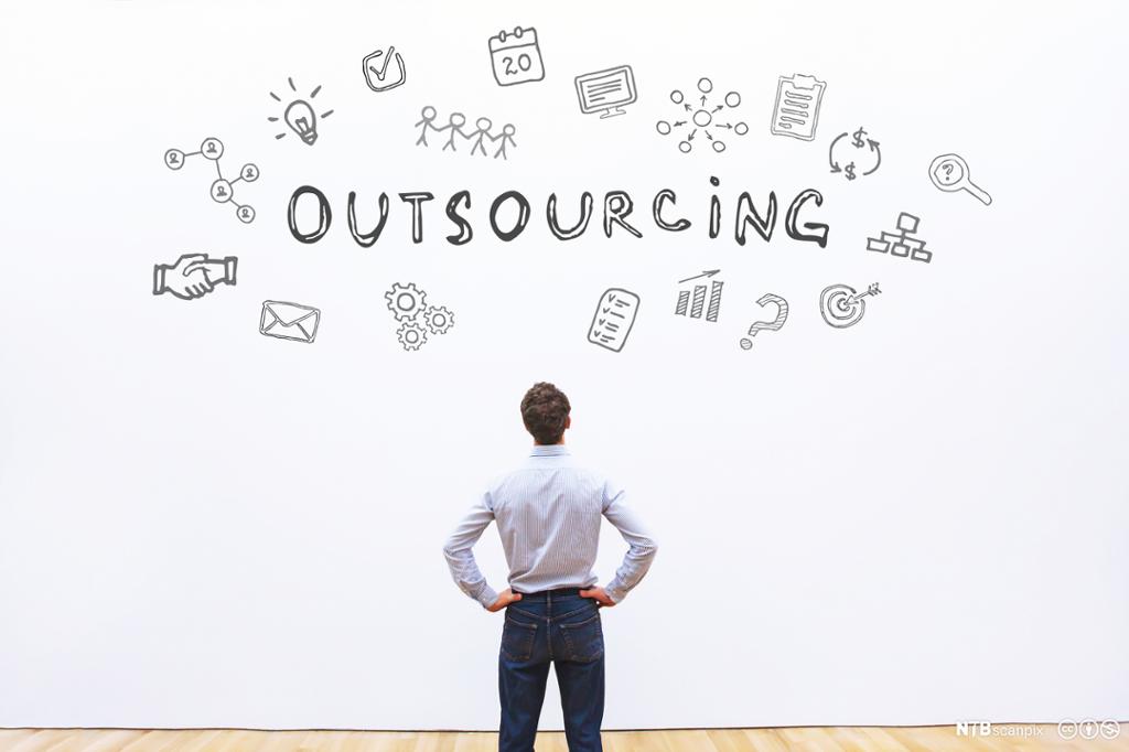 Mann står og studerer en vegg hvor det er tegninger og teksten Outsourcing. Bilde.
