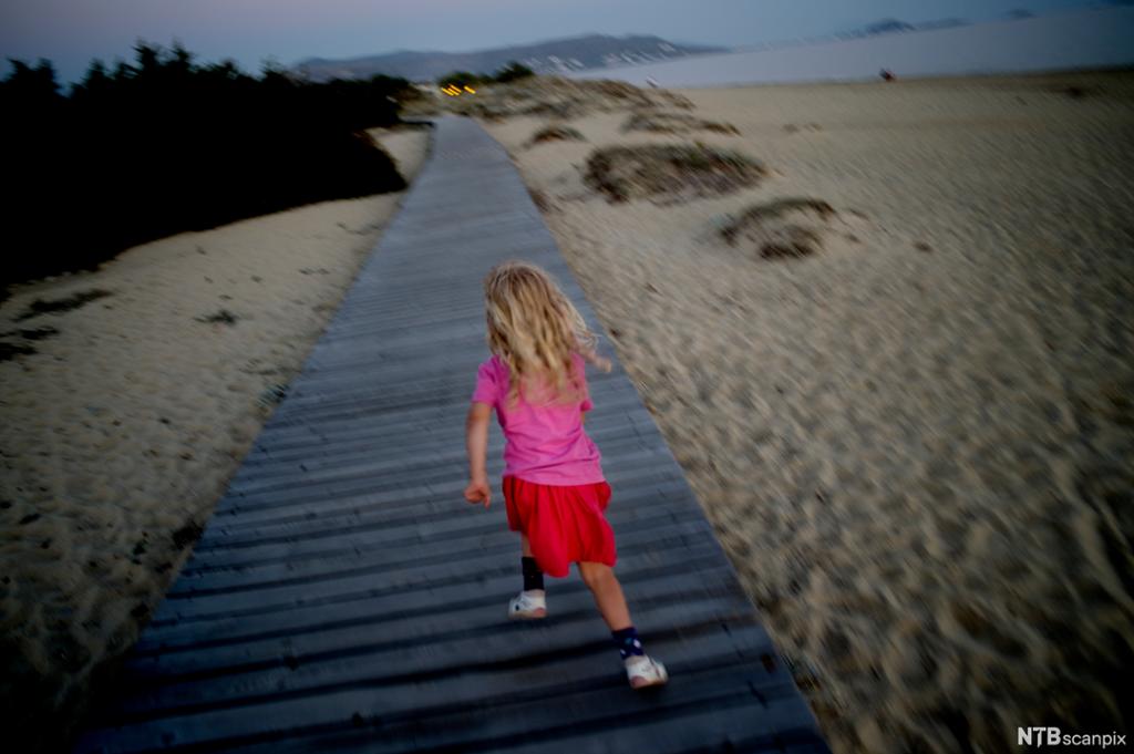 Jente løper langsmed ei strand. Foto.