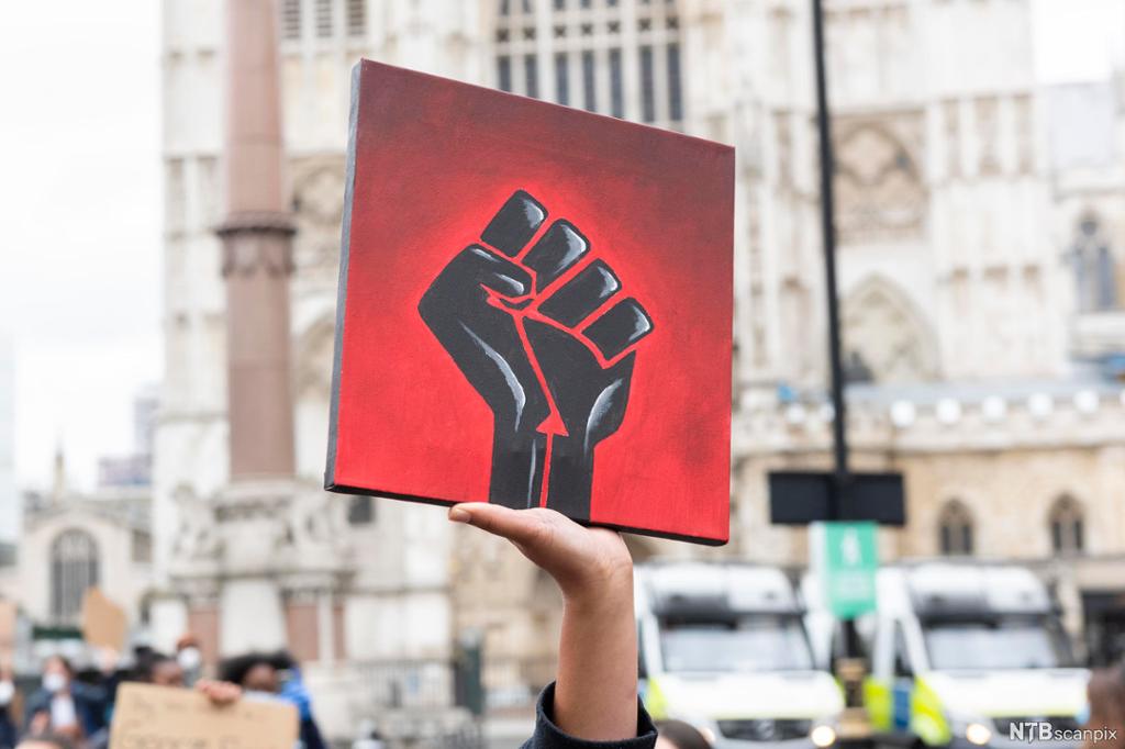 En rød plakat med en svart hånd, symbol for Black Lives Matter, under en demonstrasjon i London i 2020. Foto. 