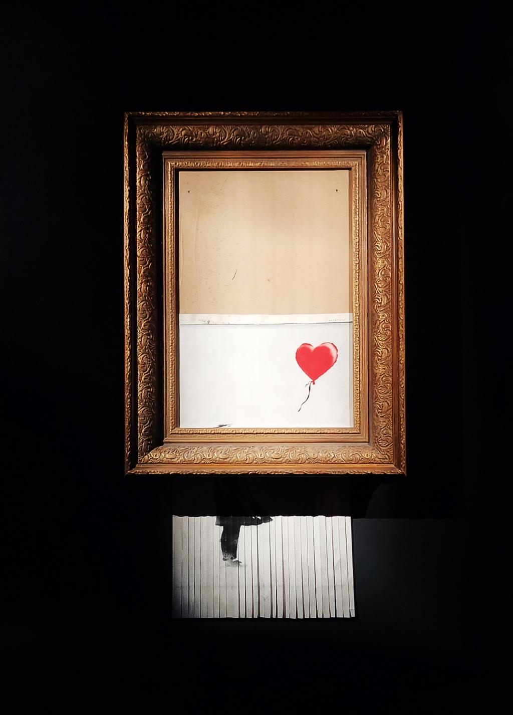 Banksy's famous picture "Girl With Ballon" has been half shredded, partly hanging out of the frame. Photo.