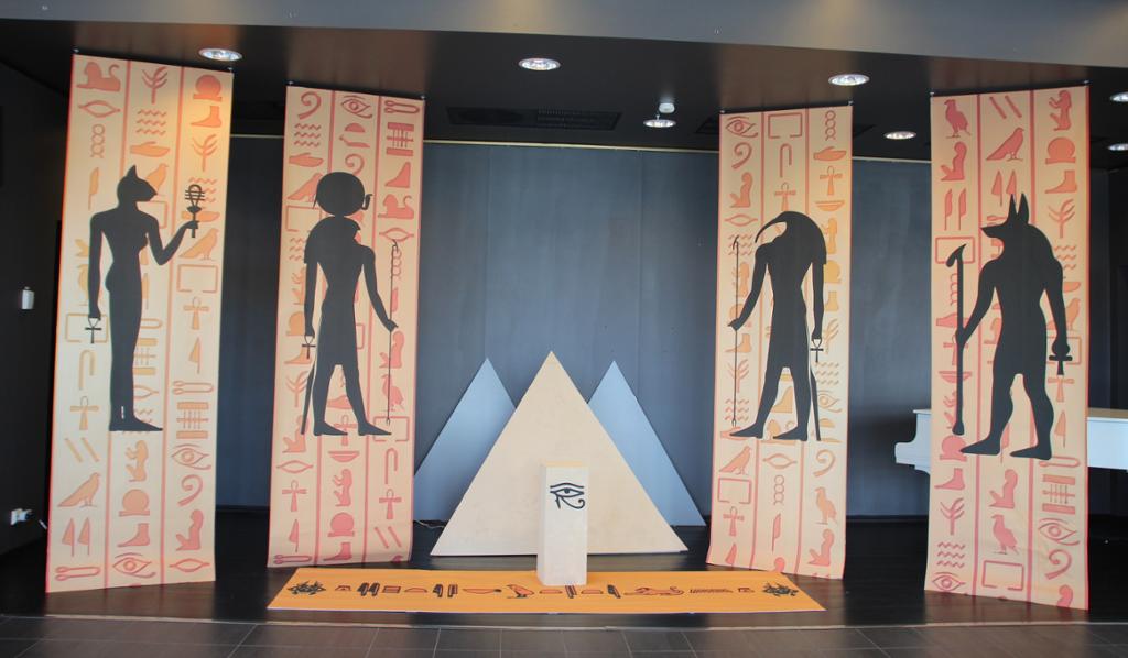 Utstilling med tre pyramider i miniatyr og fire bannere med egyptiske figurer og hieroglyfer. Foto.