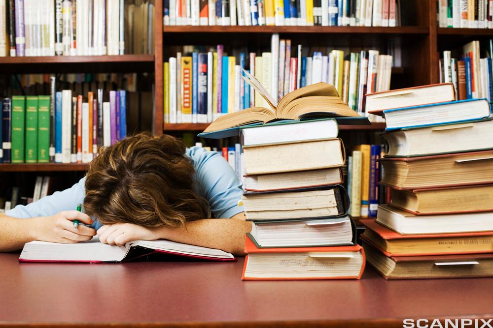 En student sover over boka si på biblioteket.