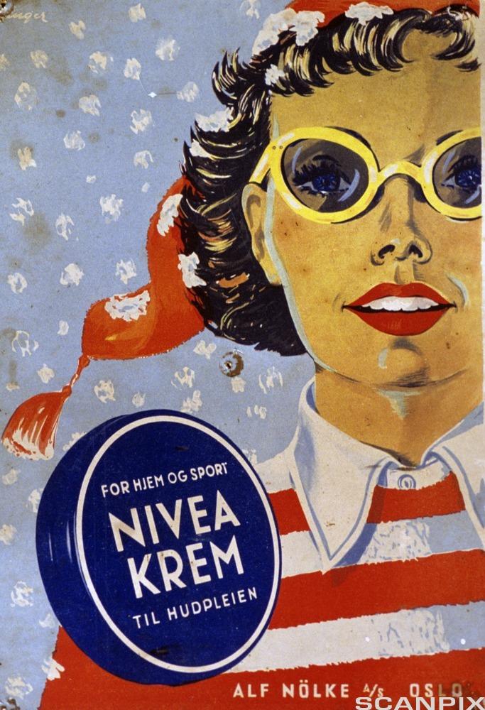 Reklameplakat som viser ei dame med gule briller. Hun har på seg rød lue og stripete genser i rødt og hvitt. Helt foran i bildet er er mørkeblå boks det det står "FOR HJEM OG SPORT NIVEA-KREM TIL HUDPLEIEN". Bakgrunnen er lyseblå med hvite snøfnugg. Illustrasjon.