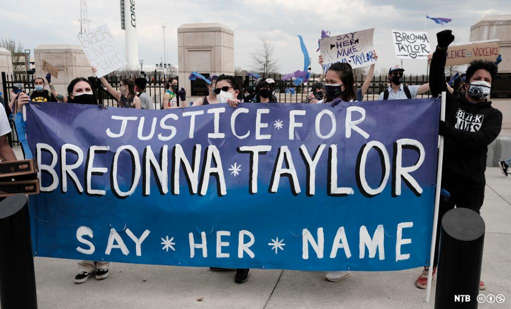 Demonstranter med munnbind holder et banner der det står "Justice for Breonna Tayler, say her name". Foto.