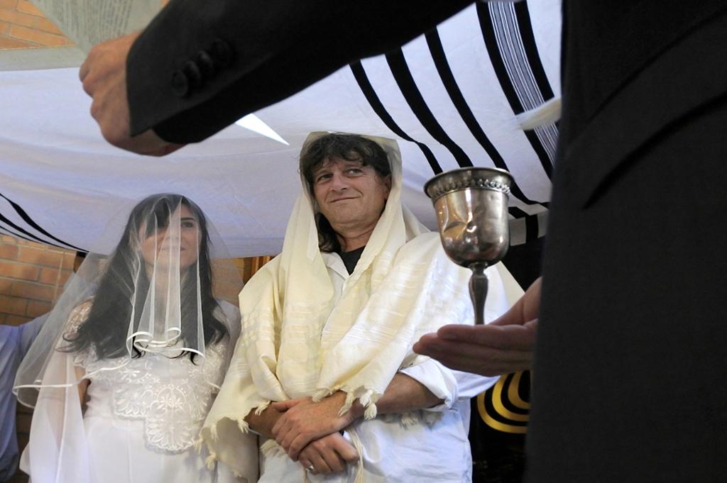 Et jødisk brudepar under en baldakin og en rabbiner som holder opp et glass vin. Foto.