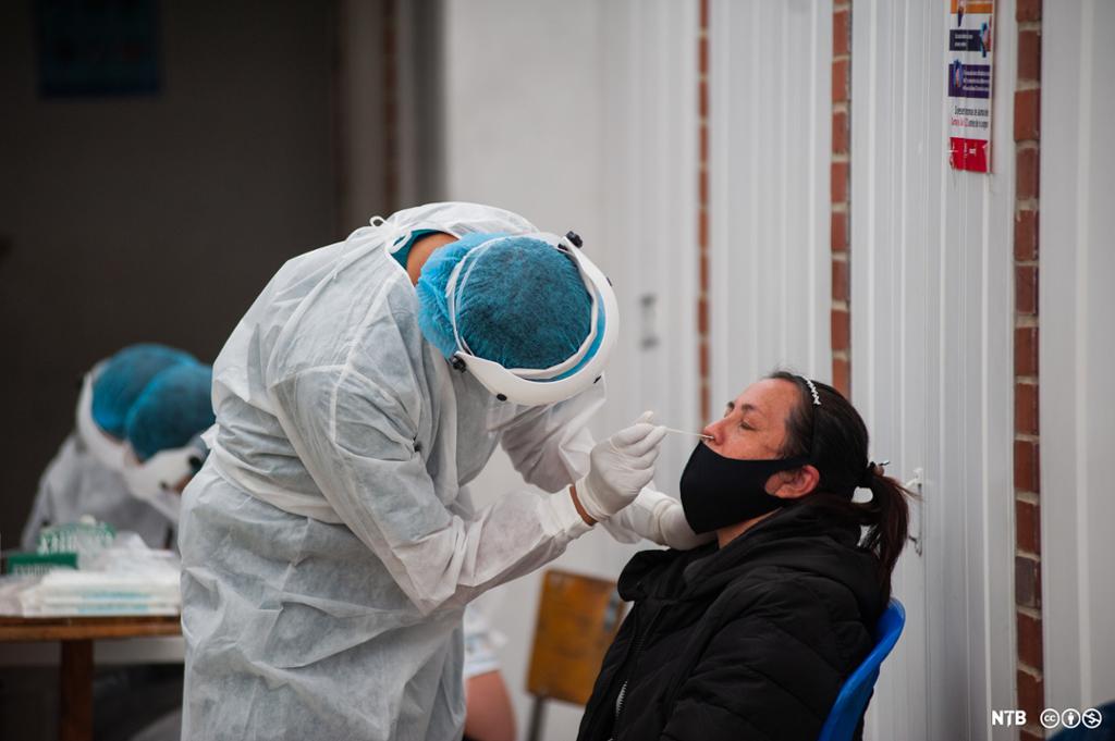 Kvinne blir testa i nasen for covid-19 av helsepersonell iført smittevernutstyr. Foto.