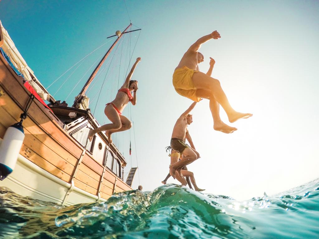 Unge mennesker hopper i havet fra seilbåt. Foto.