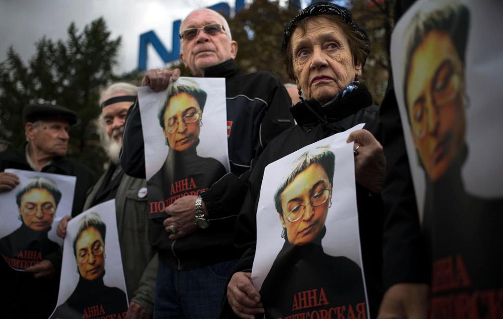 Noen menn og kvinner holder opp hver sin plakat med bilde av en middelaldrende kvinne med briller. Under bildet står navnet til den drepte journalisten Anna Politkovskaja på russisk. Foto.