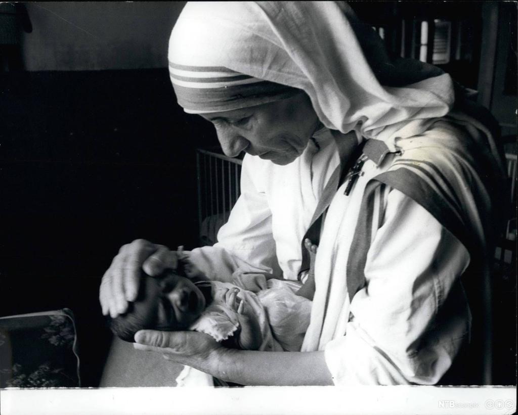 Nonne held handa på hovudet til eit spebarn. Foto.