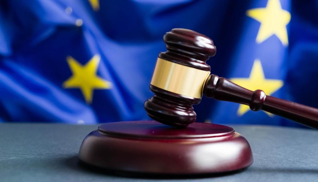 Bilde av en dommerklubbe i mørkt tre med gullfarget bånd som står på et bord med et EU-flagg i bakgrunnen.