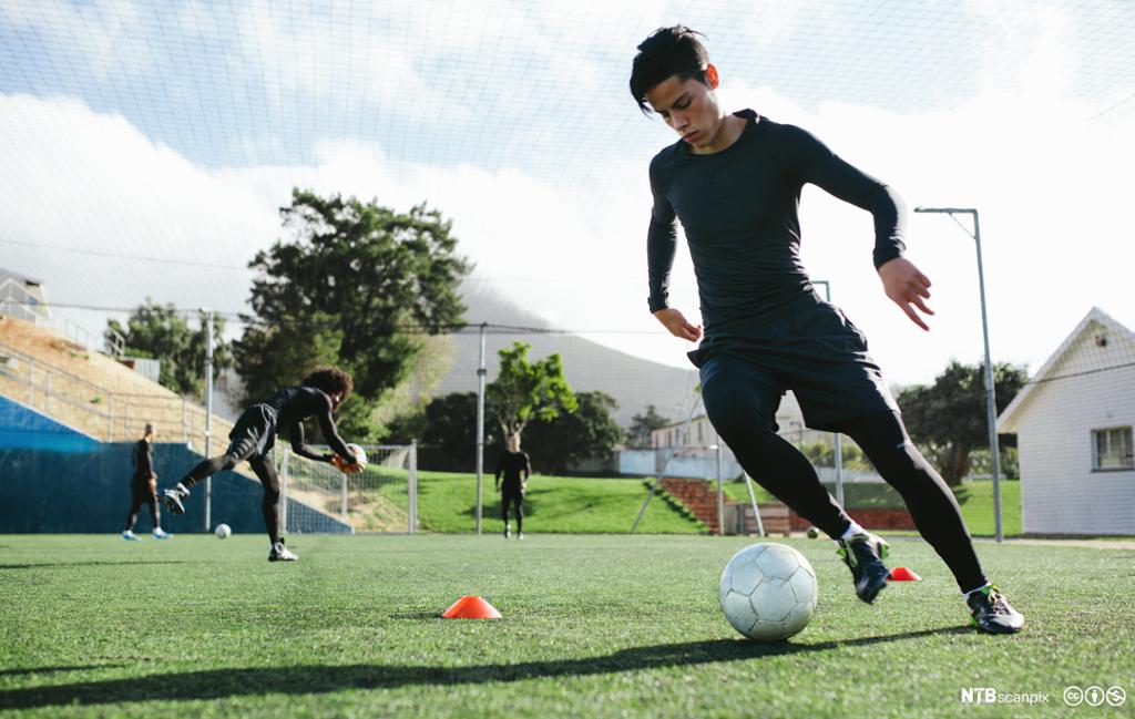Fotballspiller i trening med ball på fotballbane. Foto.