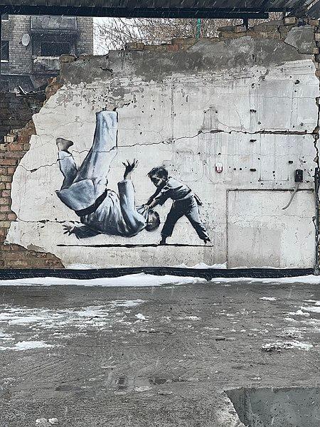 Street art by Banksy. A young boy throws Putin on the ground during a judo match. Photo.