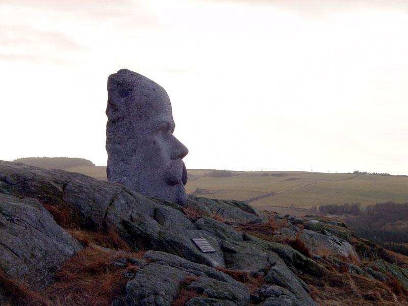 Statue av forfatteren Arne Garborg på Knudaheio. Flatt landskap på Jæren. Ansiktet hugget i stein, sett i profil. Foto. 
