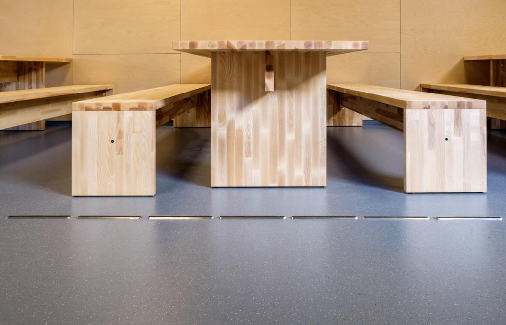 Bord og benker i tre som står på et slett gummigulv. Foto.