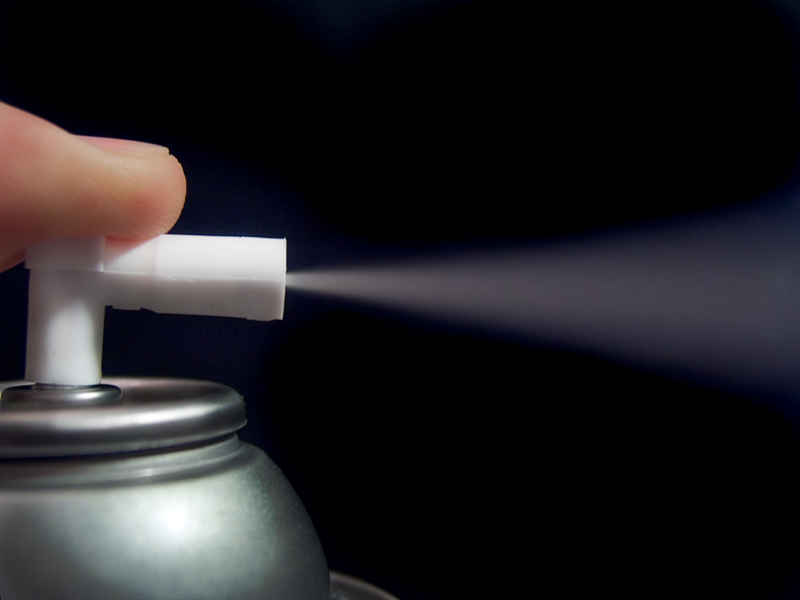 Finger trykker ned ventilen på en sprayboks. Foto.
