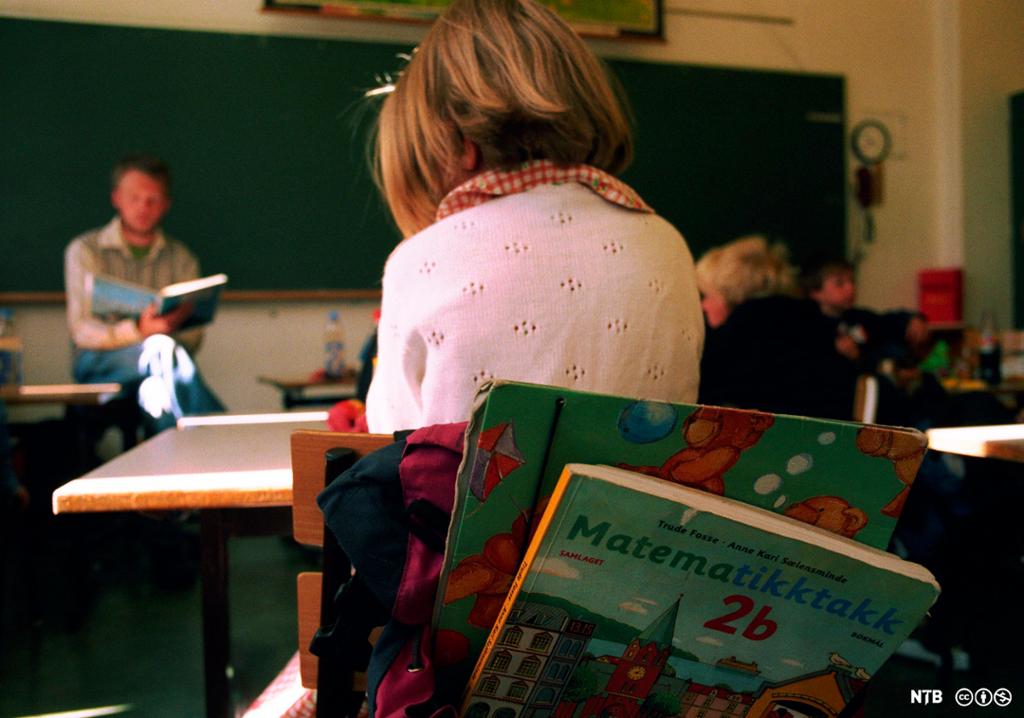Elever på andre trinn sitter ved pultene sine og lytter til en voksen som leser i ei bok. Foto.