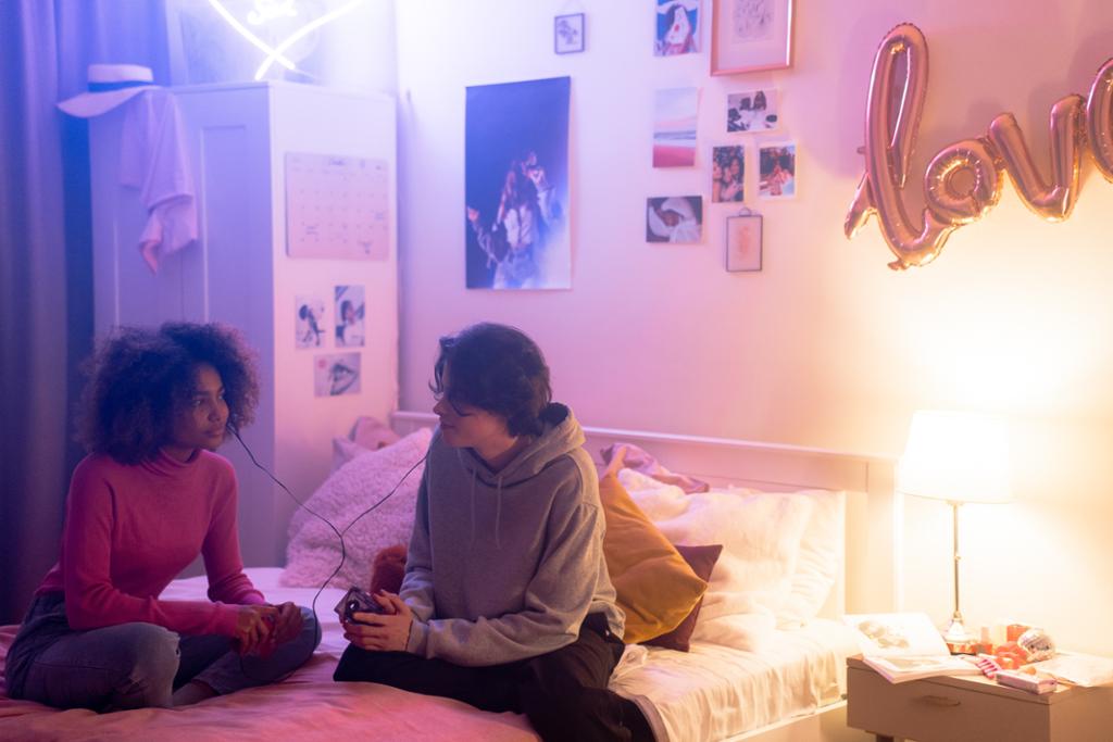 To ungdommar sit i ei seng og høyrer på musikk. Foto.